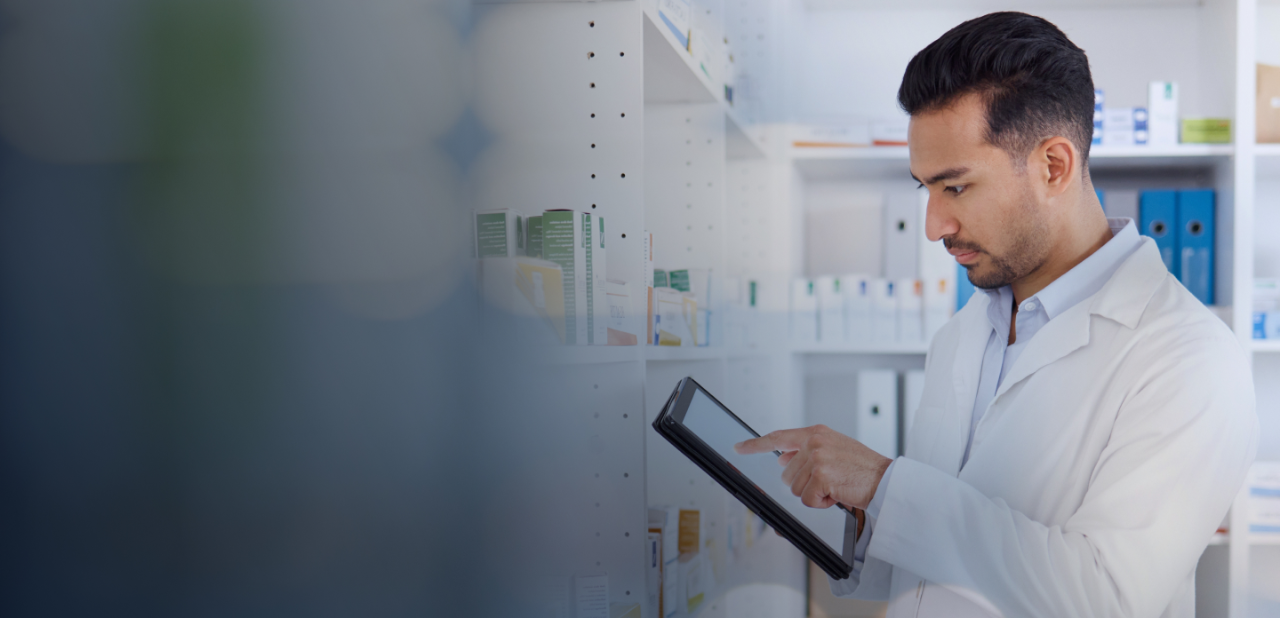Man in white lab coat touch and ipad an reviewing inventory solutions